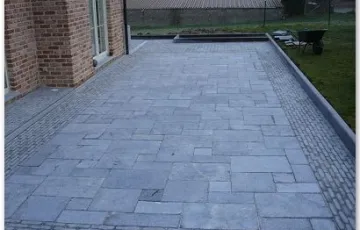 Terrasse en pierre bleue posée sur chape de sable stabilisé avec joints au sable fin + bordure en pierre bleue 100/25/8 avec bord arrondi et contour en pierre rustique 5/5/18 et l’intérieure en dalle opus romano en 4 formats.