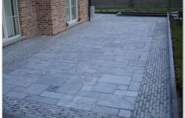 Terrasse en pierre bleue posée sur chape de sable stabilisé avec joints au sable fin + bordure en pierre bleue 100/25/8 avec bord arrondi et contour en pierre rustique 5/5/18 et l’intérieure en dalle opus romano en 4 formats.