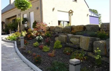 Aménagment privé avec des pavés béton rustique, bordure palissade, rocher décoratif.