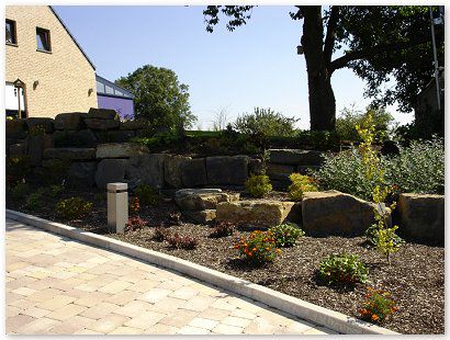 Aménagment privé avec des pavés béton rustique, bordure palissade, rocher décoratif.