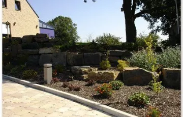 Aménagment privé avec des pavés béton rustique, bordure palissade, rocher décoratif.